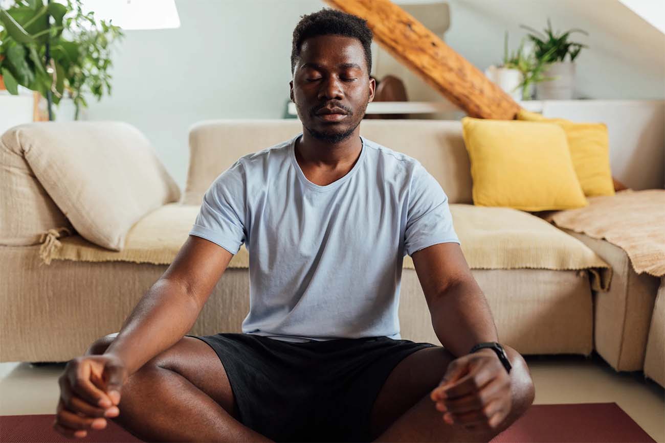 Homem fazendo meditação na sala.